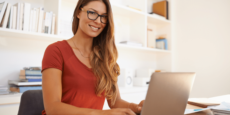 A woman wearing glasses is sitting at a desk using a laptop to find the best planners for bloggers.