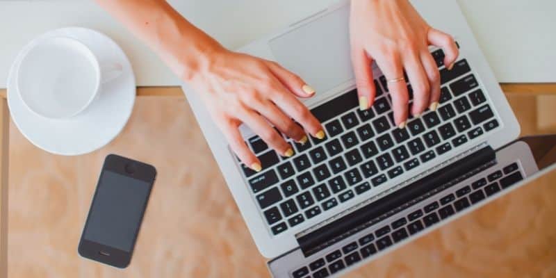 woman typing on laptop with cup 