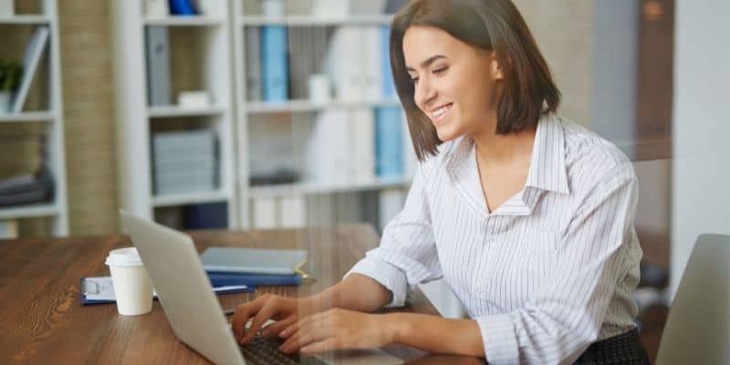 woman typing on laptop on a desk with coffee cup