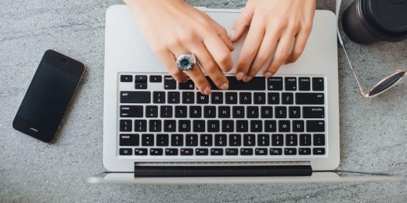 woman typing on laptop with a smartphone