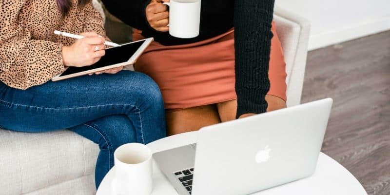 two women in front of a laptop with a tablet and coffee cup