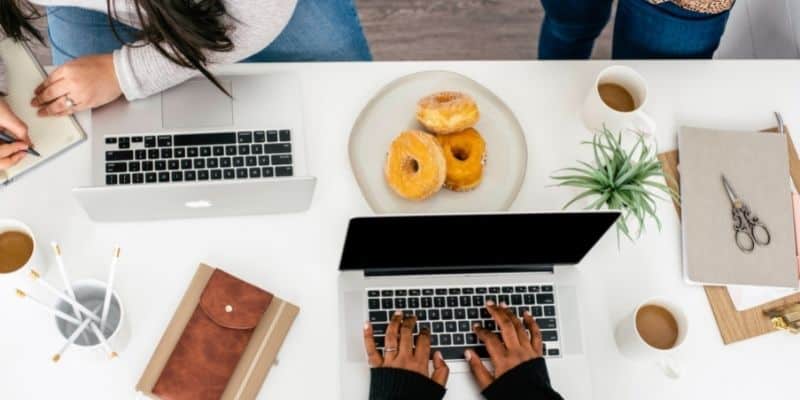 busy social media managers work on laptops with donuts and desk accessories