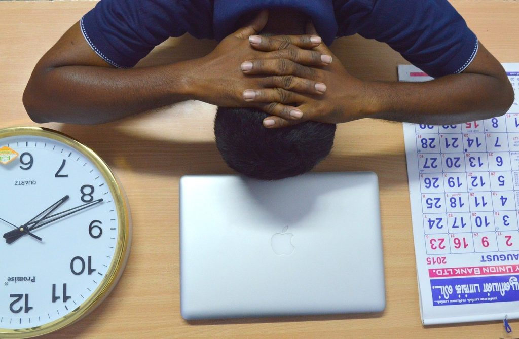 man with head down on desk, a clock, apple laptop, and calendar