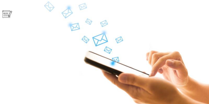 A person is holding a smartphone and typing on it. Several email icons are shown floating away from the device, symbolizing the sending or receiving of emails. A small "BLOG" icon in the top-left corner subtly hints at amateur blogging mistakes to avoid.