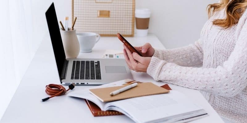 extra money for Christmas woman in white sweater on smartphone and laptop