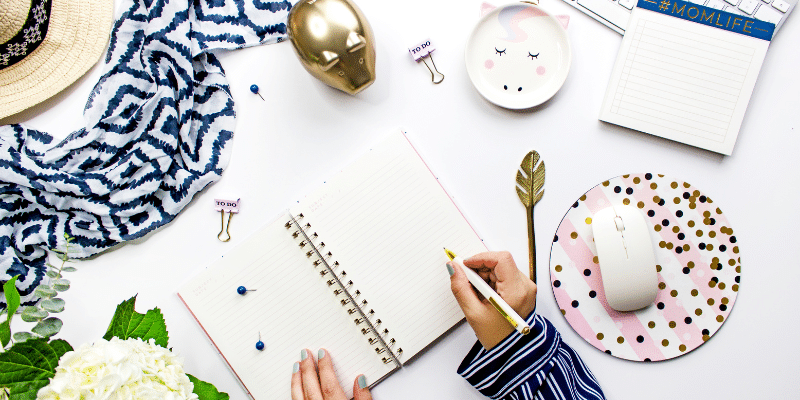 A woman is writing in a notebook, utilizing one of the best planners for bloggers.