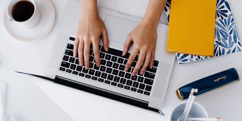 how long does it take to write 1000 words woman typing on laptop with yellow notebook