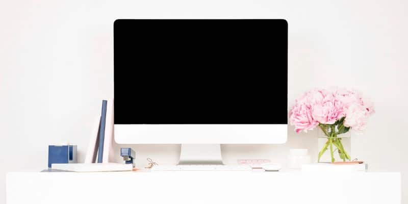 A white desk with a black screen, adorned with flowers, is an ideal space for maintaining a work-life balance.