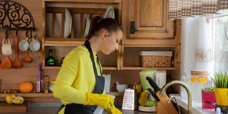 A woman maintaining a work-life balance while cleaning her kitchen with yellow gloves.