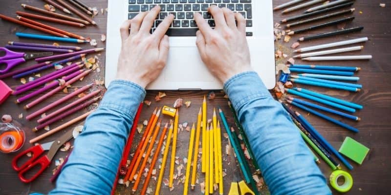 person on a laptop with colored pencils, tape, and scissors