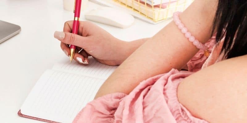  woman in pink shirt writing in a notebook