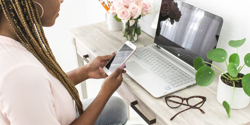 woman in a pink shirt on her phone and laptop working in her content creation framework