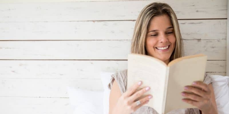 woman in bed reading book smiling