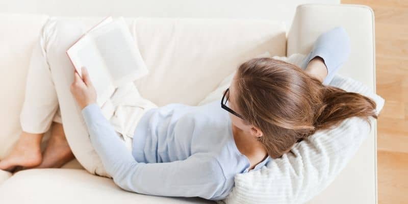 woman in blue shirt with black glasses reading on couch