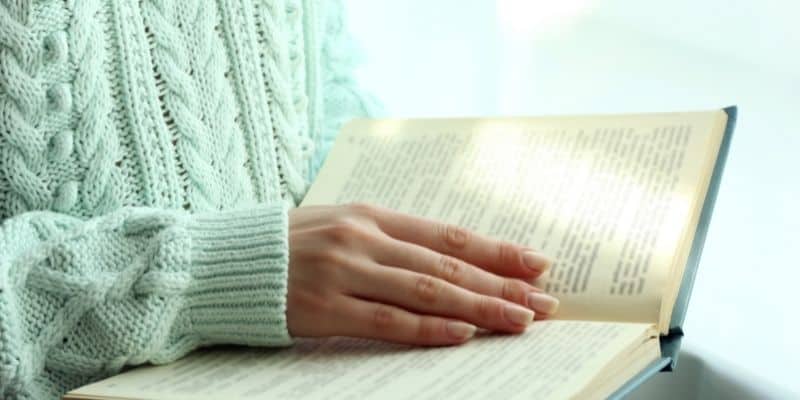 woman in green sweater with hand over book