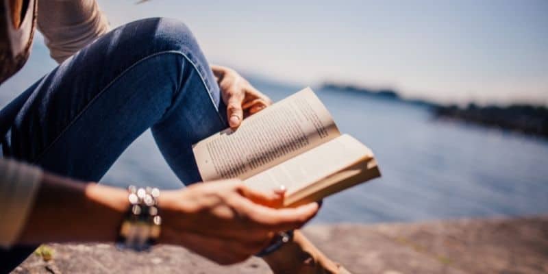 woman in jeans reading book by the beach