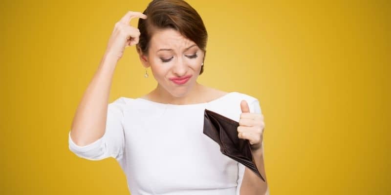 woman in white scratching head with an empty wallet