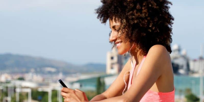 woman outside in pink shirt listening to headphones with phone in hand