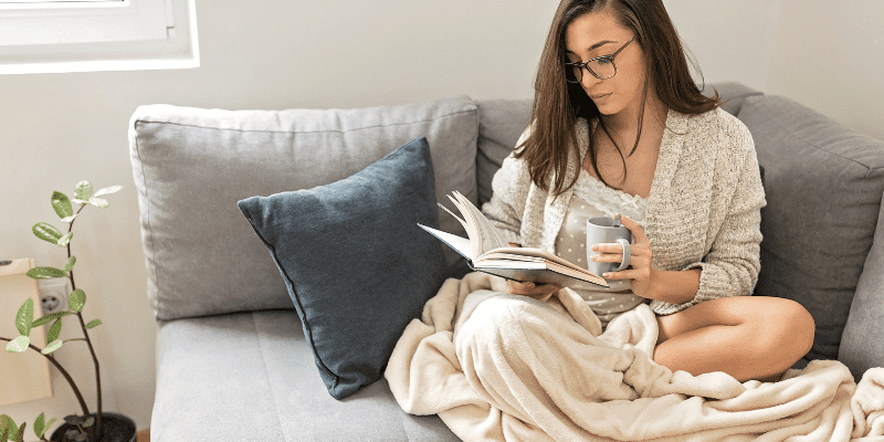 woman reading book on ouch with coffee