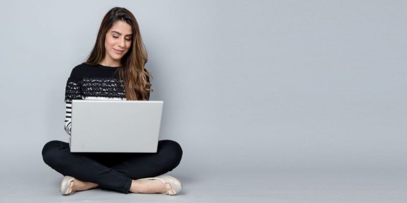 woman sitting down with laptop grey background