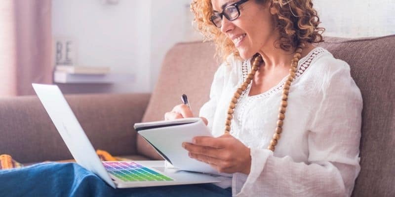 woman sitting on couch with computer and notebook, and pen