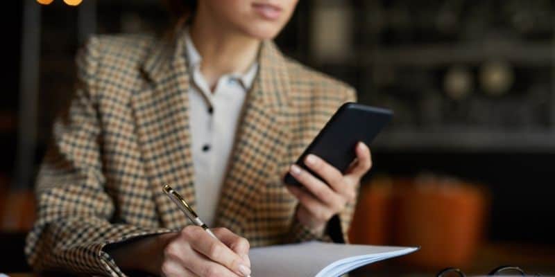 woman sitting writing with pen and phone in hands