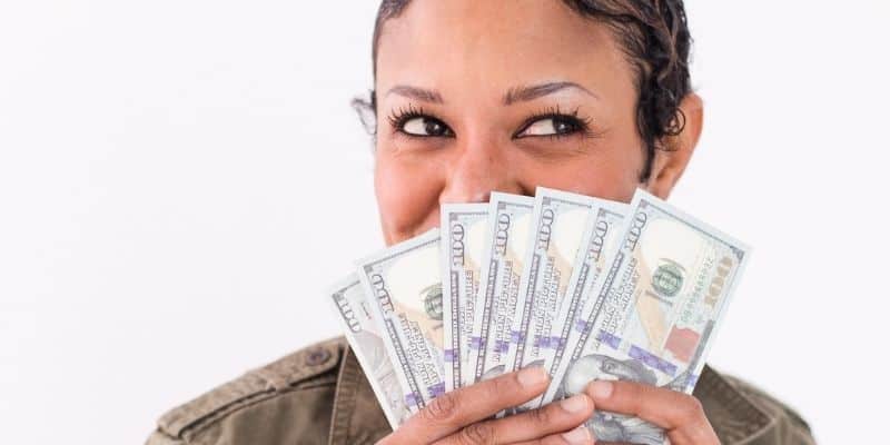 woman smiling with hundred dollar bills fanned out in hands