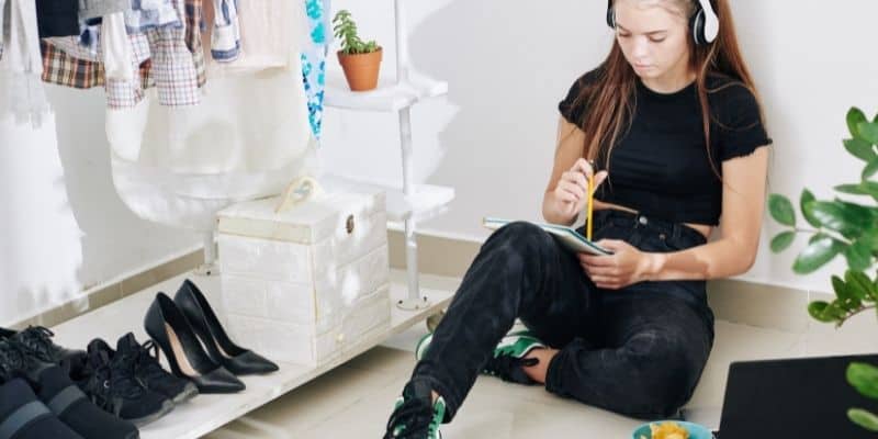 woman wearing all black and headphones writing in notebook