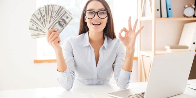 woman with glasses with a fan of money and laptop