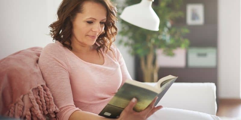 woman with pink shirt reading book on couch