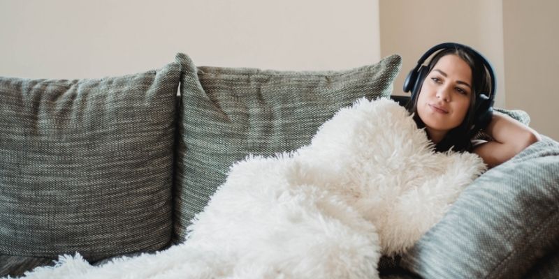 woman wrapped in blanket laying on couch listening to audio book