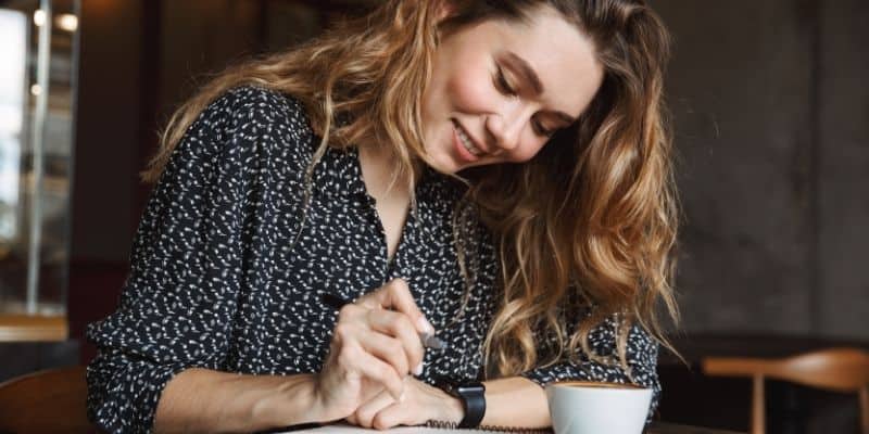 woman writing on table with coffee