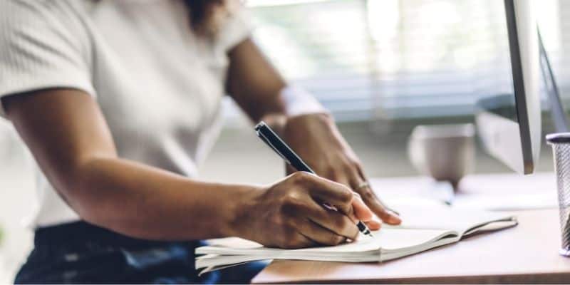 woman writing on table with notebook and pen