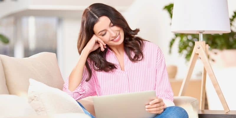 woman in pink shirt sitting on couch with computer