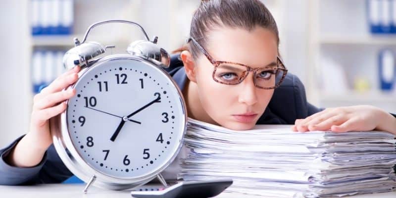 work from home successfully woman with head on stack of papers, crooked glasses and big clock